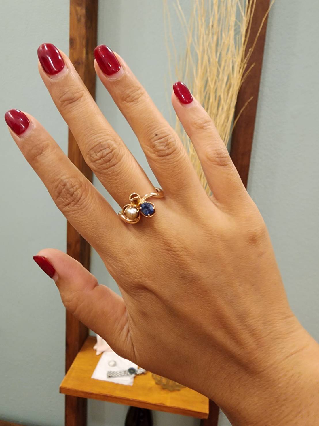 A finished sapphire ring worn on a hand with deep red nails.