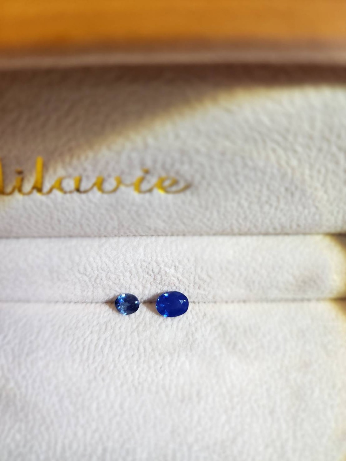 Two polished blue gemstones resting on a pale jewelry surface.