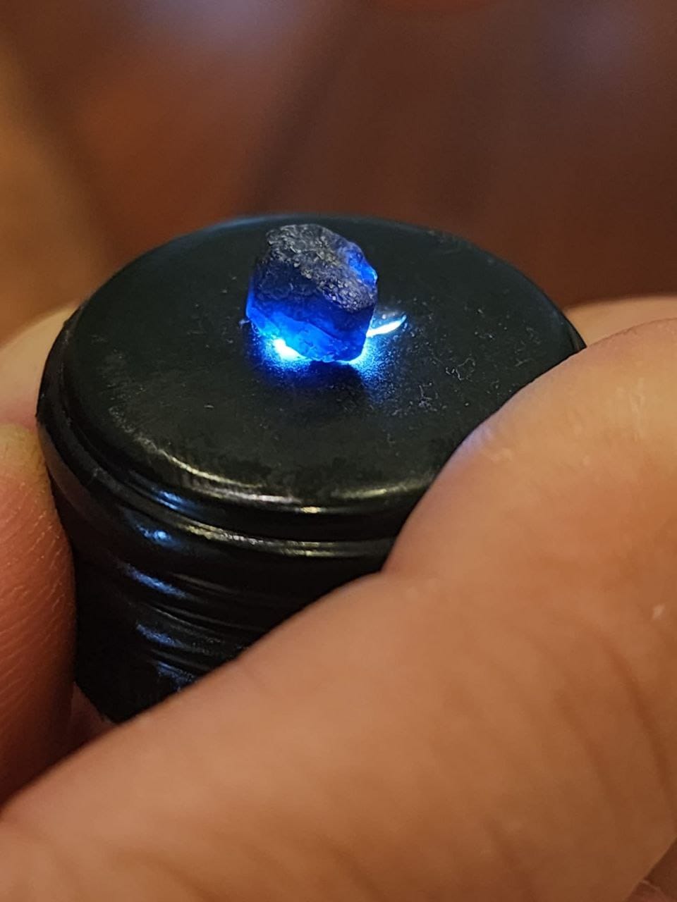 A rough blue gemstone glowing on a small inspection light.