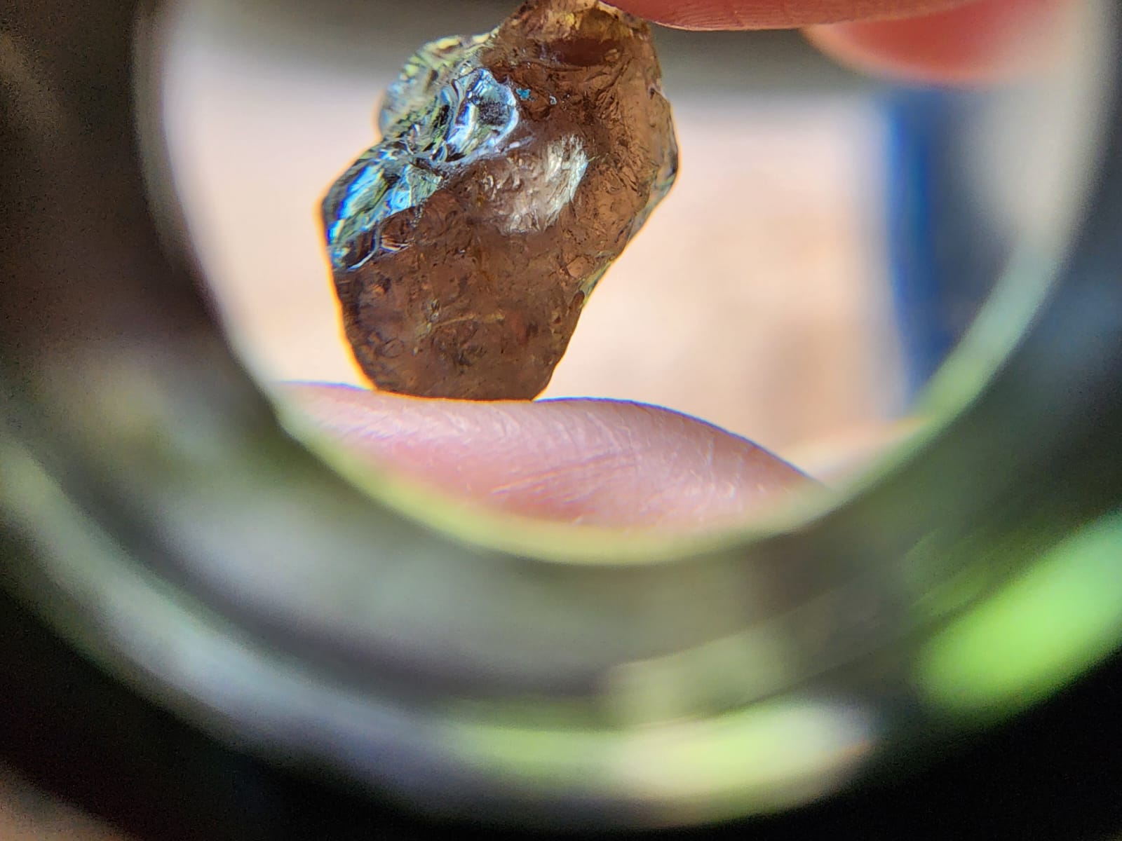 A rough amber-brown gemstone inspected through a magnifying loupe.