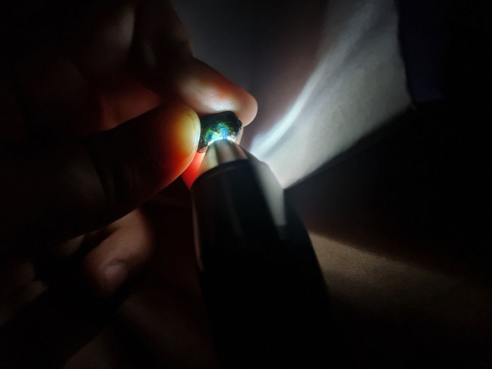 A rough blue gemstone being inspected with a handheld light in darkness.