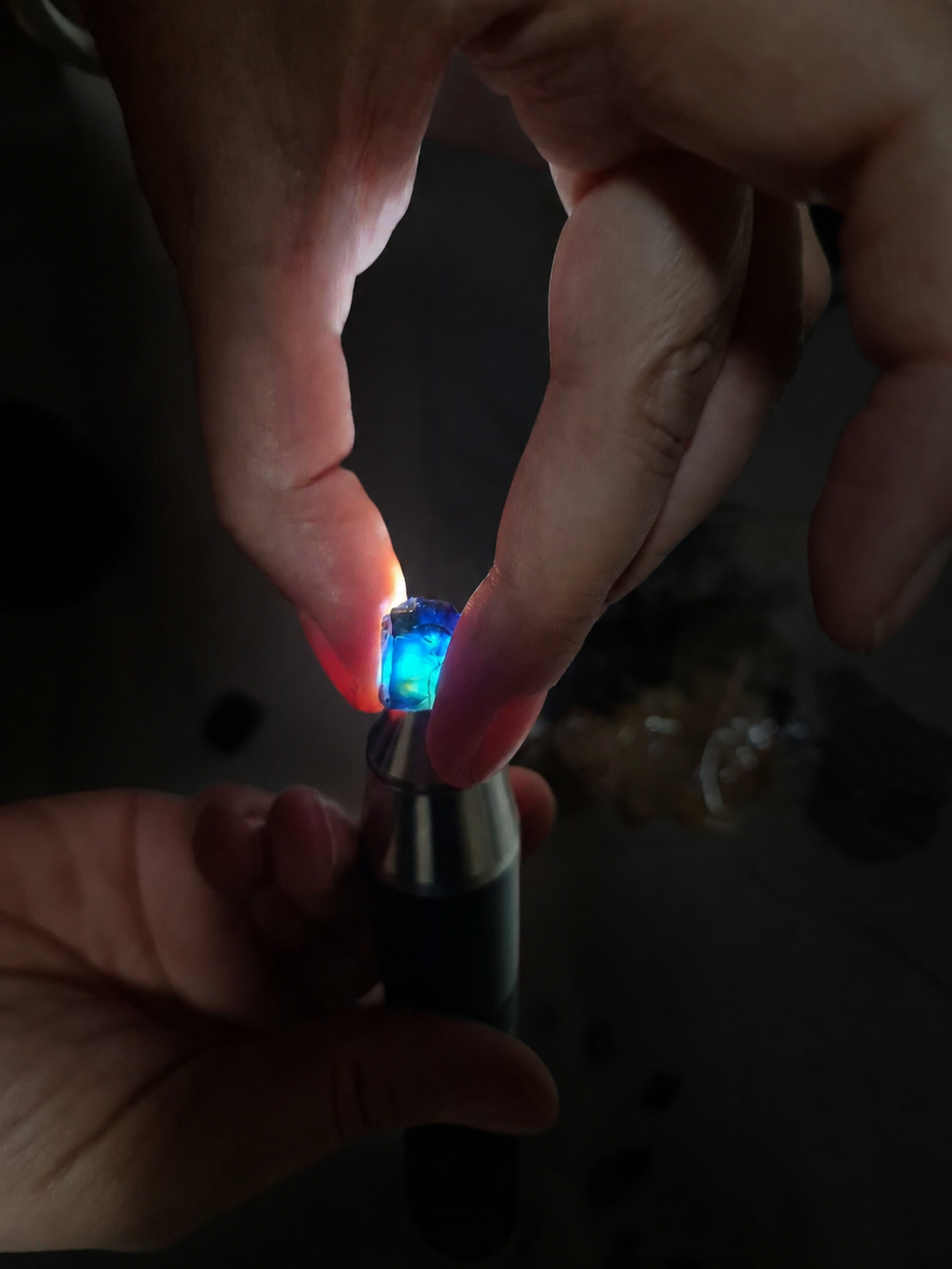 A real blue gemstone held between fingers while being illuminated from below with a small inspection light.